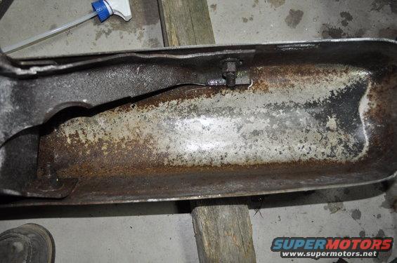 Rusted metal part with a crack, supported by wooden blocks. A spray bottle is visible in the background