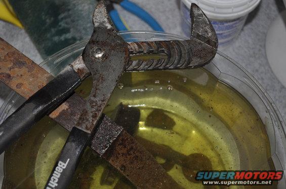Rusted metal parts soaking in yellow liquid, with pliers and a chisel visible