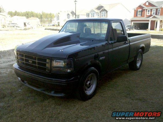 Black pickup truck with a large aftermarket hood and custom wheels parked on grass