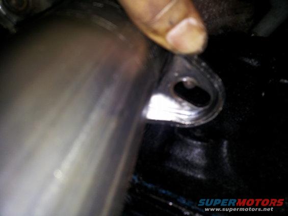 Close-up of an exhaust pipe connection with a finger pointing to a flange