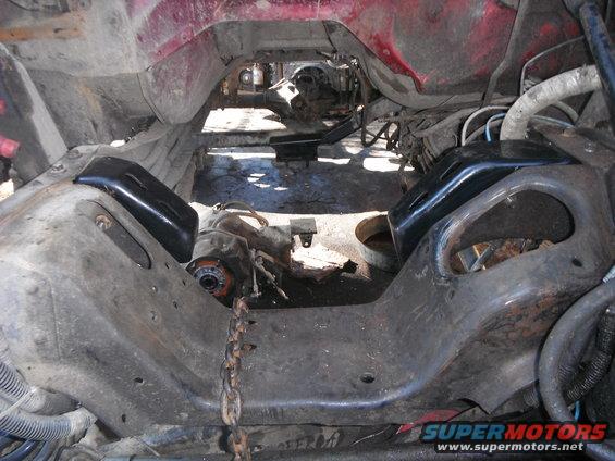 Vehicle frame with engine mounts and drivetrain components visible, red bodywork above, chain in foreground