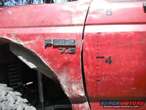 Red truck fender with F-Super Duty 7.5 badge, dented. Door has height markings