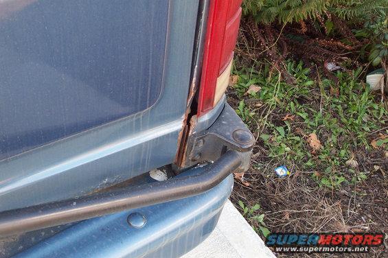 Blue SUV rear corner with visible rust around the taillight and bumper
