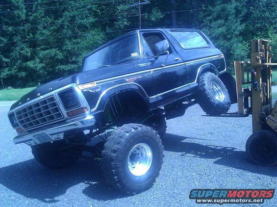 Lifted black Ford Bronco with large tires, front end is elevated by a forklift