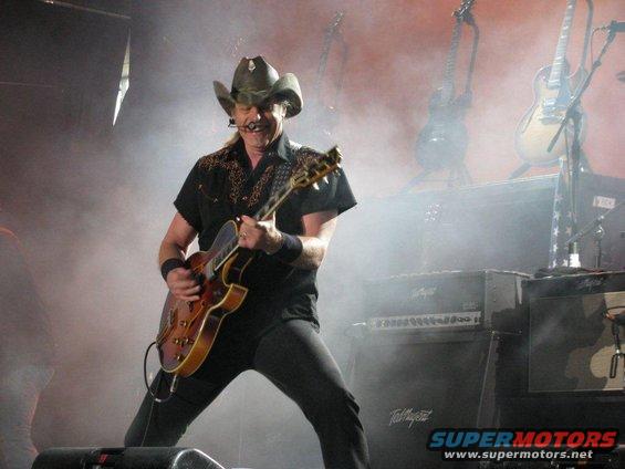 Musician in cowboy hat playing guitar on stage with smoke and lights