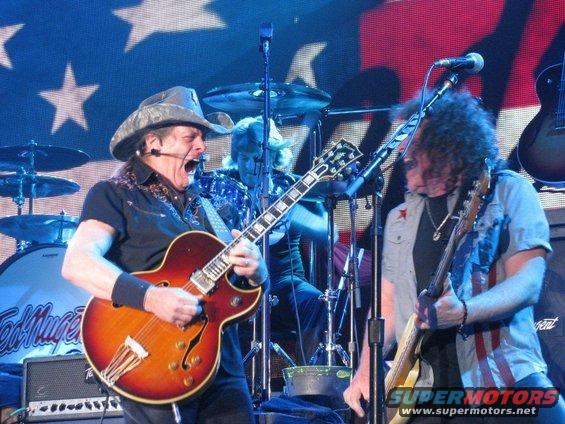 Ted Nugent and another guitarist perform on stage with a drum kit behind them