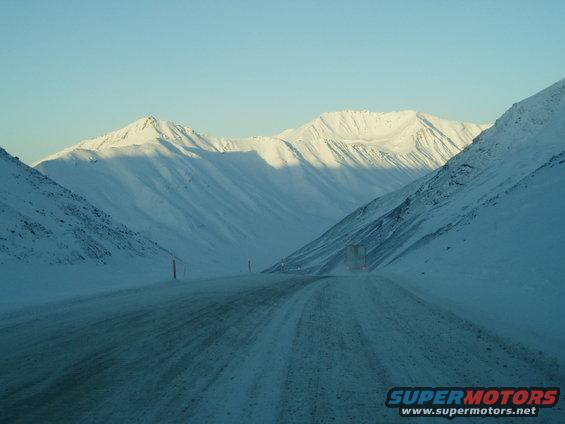 Truck driving on a snowy mountain road under a clear blue sky