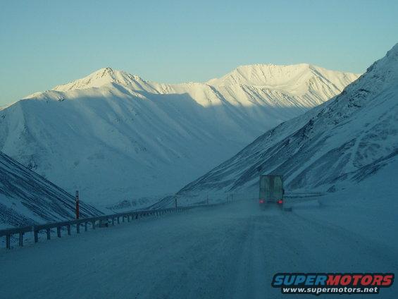 Truck driving on a snow-covered road with mountains in the background
