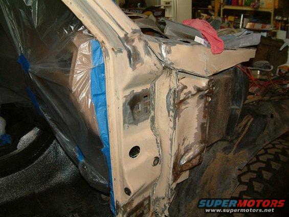 Close-up of a vehicle's bodywork undergoing repair, with plastic sheeting and blue tape covering parts of the frame