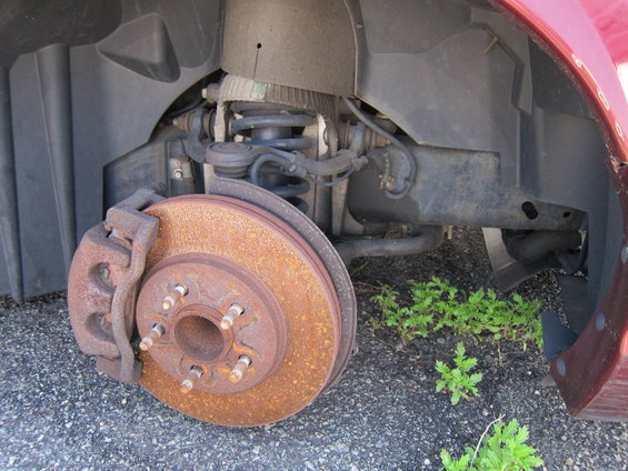 Close-up of a rusty brake rotor and suspension components on a vehicle