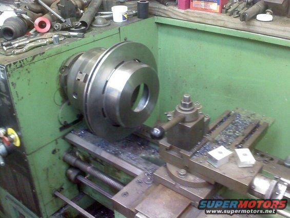 Metal brake rotor being machined on a lathe with metal shavings on the machine bed