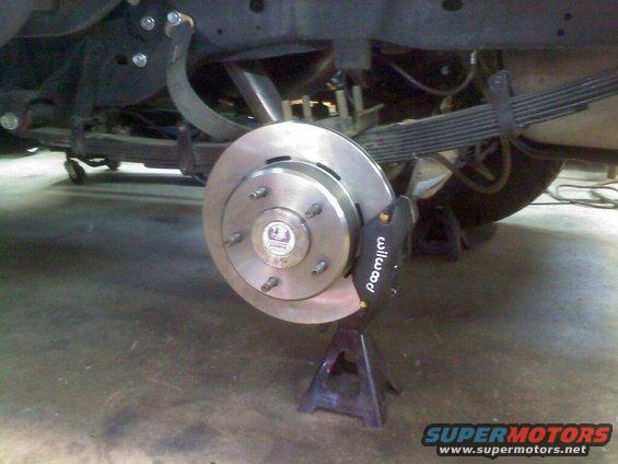 Close-up of a vehicle's rear brake rotor and caliper assembly, supported by jack stands