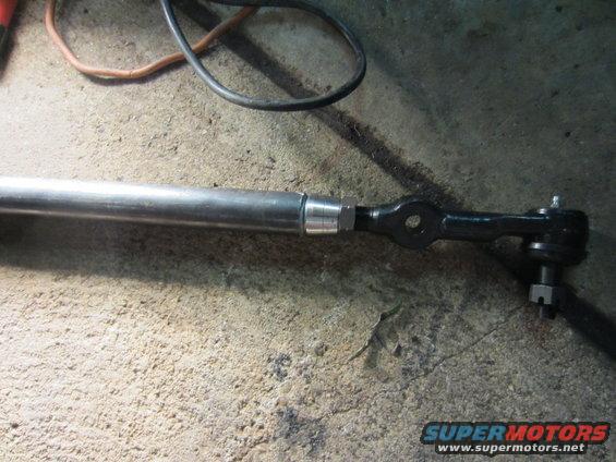 Steering linkage rod with tie rod end attached, resting on concrete