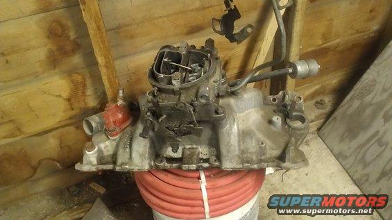 Engine intake manifold with carburetor, silver, mounted on a red hose coil