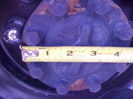 Wheel hub with six lug nuts and a yellow measuring tape showing approximately 3 inches