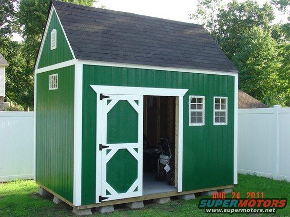 Green shed with white trim and double doors. Lawn mower inside