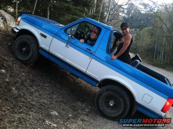 Blue and white Ford F-150 pickup truck on a dirt incline with two people inside