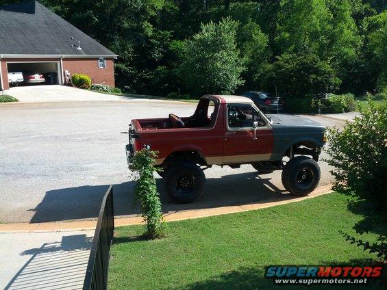 Lifted Ford Bronco with red and gray body panels, large off-road tires, parked in a driveway