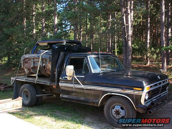 Black flatbed truck with a car body on its bed. The truck appears to be a 1973 Ford F-Series