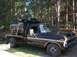 1974 Ford F-350 - A black flatbed truck is transporting a car body, possibly a 1973 Ford F-Series, through a wooded area.