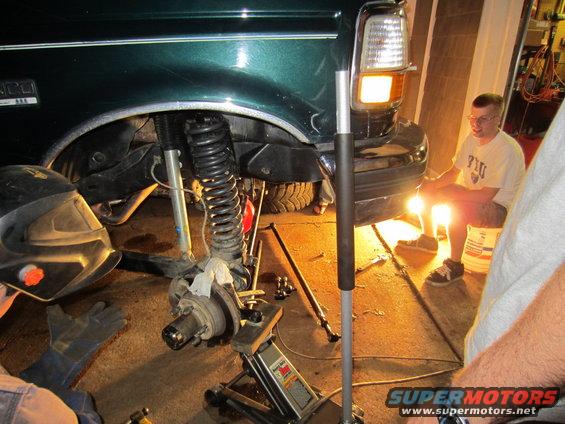 Green 1992 Ford Bronco front wheel assembly being worked on, jacked up, with a person welding