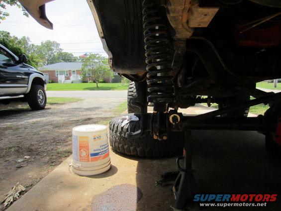 Undercarriage of lifted vehicle with suspension components visible. Another truck is parked nearby