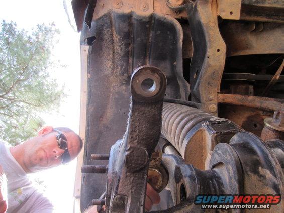 Close-up of vehicle steering linkage and suspension parts, with a man in sunglasses looking on