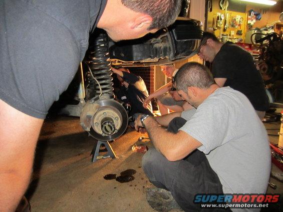 Front suspension and brake assembly on jack stands, mechanics working