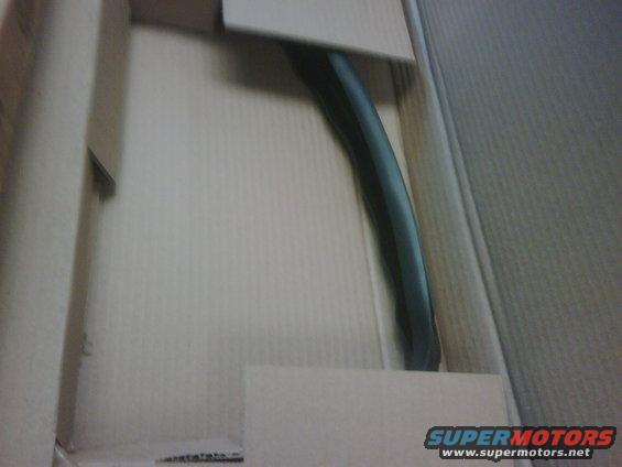 Black curved car part inside a cardboard box