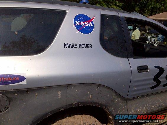 Silver SUV side view, mud-splattered, with NASA and MARS ROVER decals. Number 33 visible
