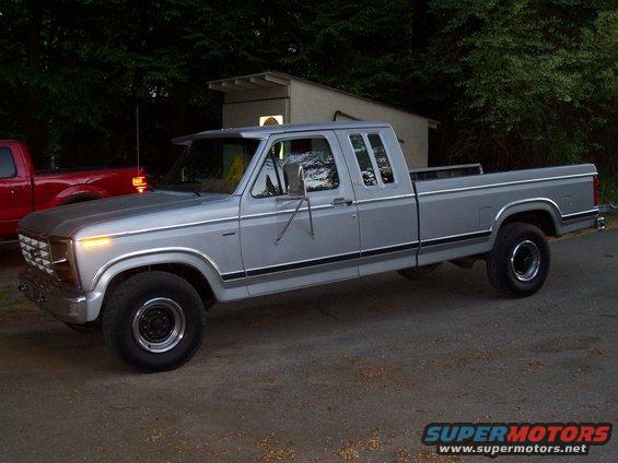 Silver crew cab pickup truck parked next to a red truck. It has a long bed and chrome trim
