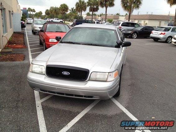 Silver Ford Crown Victoria parked in a lot. Other cars are visible in the background