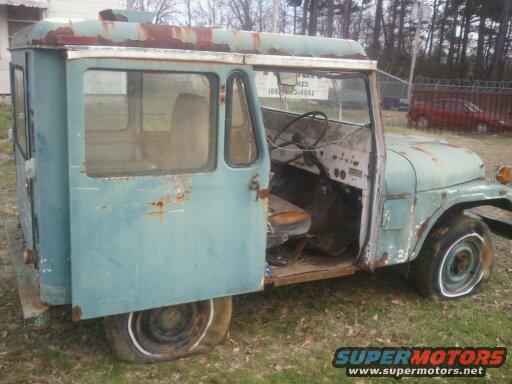 Old teal Jeep panel van with flat tires and rust, driver's door open