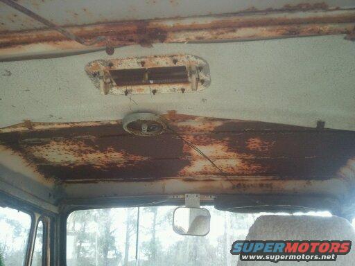 Interior view of a heavily rusted vehicle's headliner and dashboard area, showing a rearview mirror and a vent