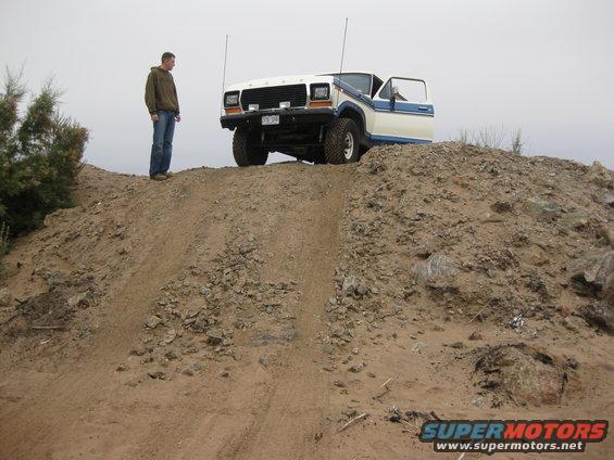 White and blue 1979 Ford Bronco parked on a dirt hill with driver's door open