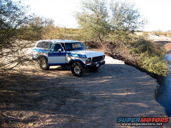 1979 Ford Bronco with blue and white paint parked on a dirt embankment next to water