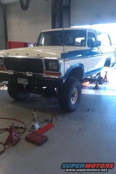 White and blue 1979 Ford Bronco on jack stands in a garage