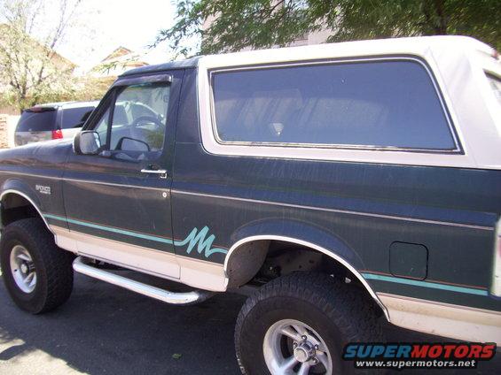 Dark green 1993 Ford Bronco side view with white top and teal stripe