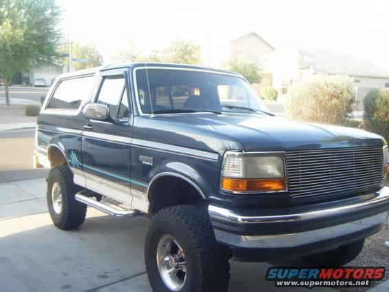 Dark blue Ford Bronco with chrome grille and side steps, lifted on large tires