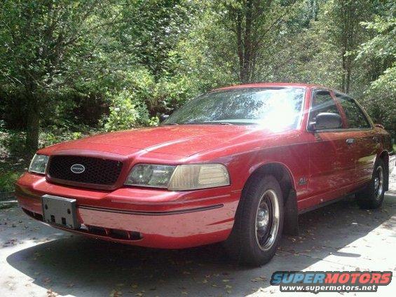 Red 2000 Ford Crown Victoria parked outdoors with trees in the background