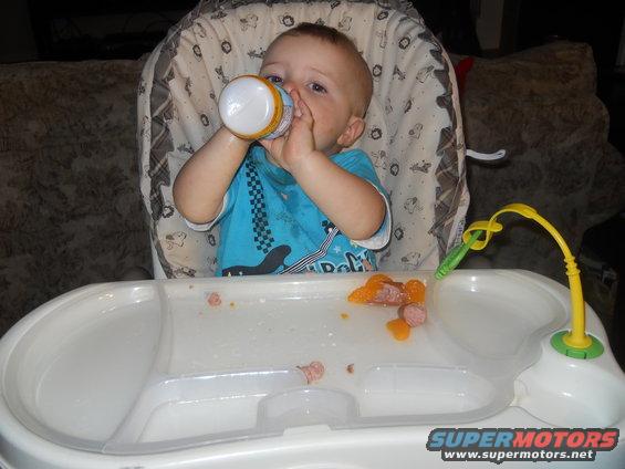 Baby in high chair drinking from bottle, food on tray
