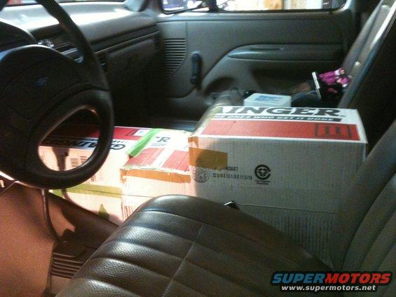 Interior of a vehicle with boxes stacked on the passenger seat and floor. The steering wheel and dashboard are visible