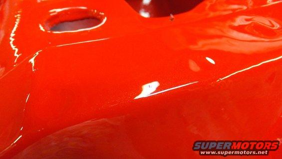 Close-up of a shiny red painted metal part with two circular indentations