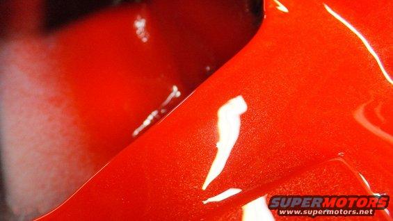Close-up of a shiny red painted metal surface with reflections