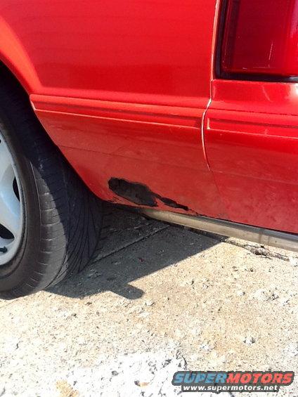 Red car side panel with rust near the wheel well and a chrome trim piece