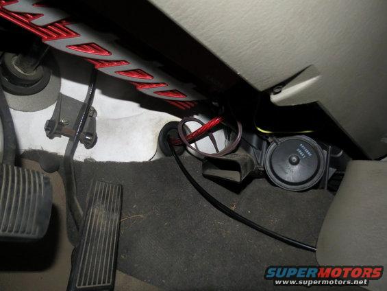 Vehicle interior showing brake and gas pedals, black wiring, and a circular black component