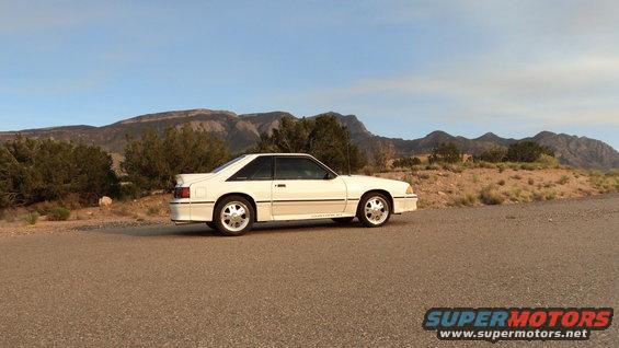 White coupe car parked on a dirt road with mountains in the background