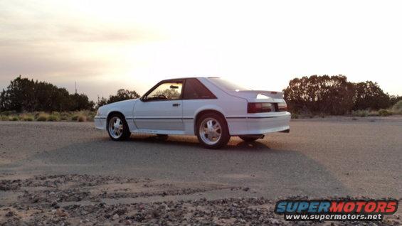1989 Ford Mustang coupe parked on dirt road with trees in background