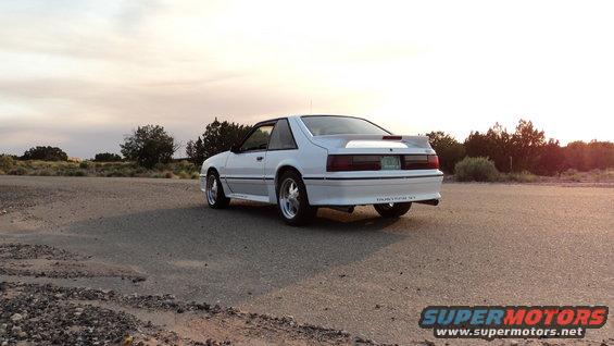 White Ford Mustang GT parked on a dirt road at sunset, rear view