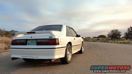 White 1989 Ford Mustang GT parked on a dirt road with mountains in the background